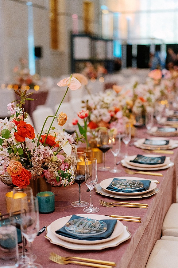 Reception tablescape with a wedding floral centerpiece, taper candles, and gold flatware, set on round tables in a softly lit indoor room