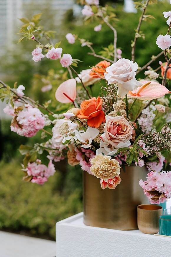 Wedding floral arrangement on a ceremony floral pedestal with roses, cherry blossom branches, and anthurium in a bronze vase with votive candles