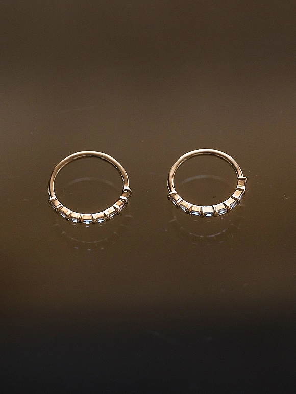 Wedding rings in a wedding band set resting on a reflective dark surface, showing sleek metal shine and subtle mirrored reflections