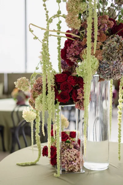 Wedding centerpiece tall wedding centerpiece of red roses and hydrangea with hanging amaranthus in a clear water-filled cylinder vase on linen table