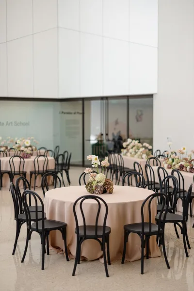 Reception tablescape with round wedding reception tables in blush linens, black bentwood chairs, and hydrangea centerpieces in a modern glass-walled venue