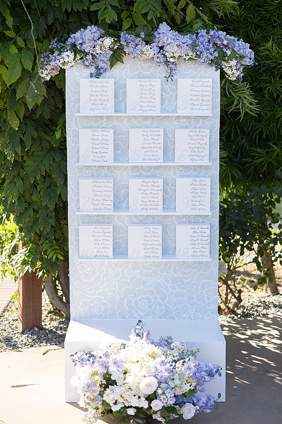 Wedding seating chart with alphabetical seating chart cards in calligraphy on a white board, framed by blue florals along a garden pathway