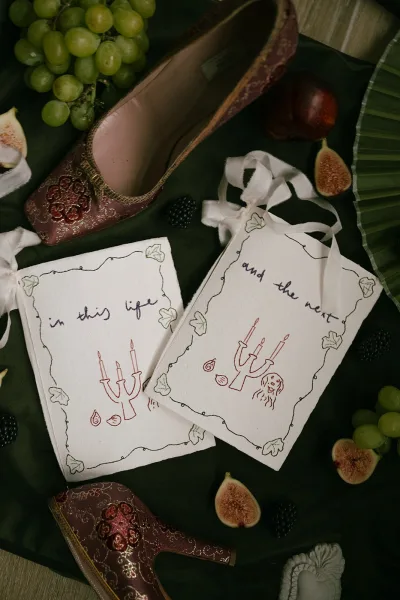 Wedding vow books in a vow booklet set arranged on green fabric, a single fig accenting the flat lay as wood floor peeks along the edge.
