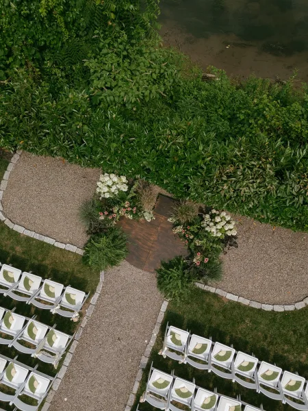 Outdoor ceremony setup along a garden ceremony aisle with hand fans on the chairs, overlooking a calm riverbank.