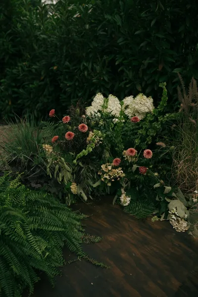 Ceremony aisle flowers shape a grounded floral aisle with white hydrangeas, set against garden hedges.