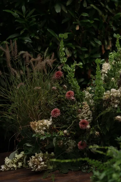 Floral arrangement of garden-inspired florals with mauve blooms, resting on a wooden surface with soft garden foliage.