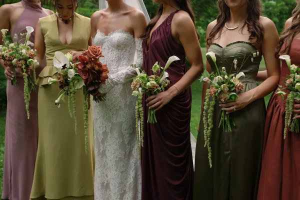 Bridesmaid dresses take center stage as mismatched bridesmaid dresses in earth tones frame the bride with calla lily bouquets in a lush garden