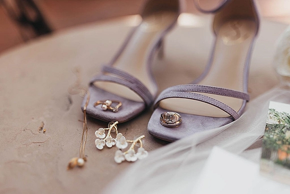 Wedding shoe flatlay with bridal shoes flatlay featuring strappy heels, rings, pearl drop earrings and tulle on a stone surface with a printed photo