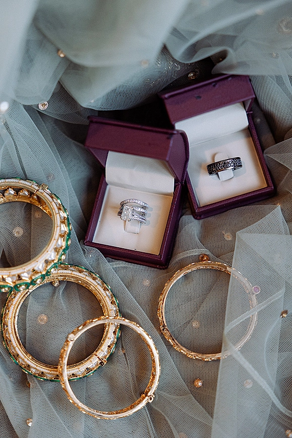 Wedding rings arranged in a wedding ring flat lay with ring boxes and bangles on beaded tulle fabric against a soft backdrop