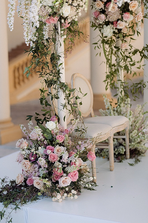 Wedding ceremony altar with ceremony floral pillars draped in pink and white roses and greenery, framed by stone staircase steps outdoors
