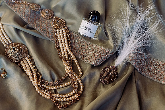 Bridal accessories flat lay with pearl wedding jewelry, crystal necklace, brooch, perfume bottle and ring arranged on draped satin fabric