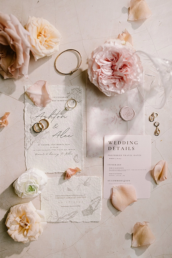 Invitation suite wedding invitation flatlay with deckled cards, blush wax seal, gold rings, pearl earrings, and pink peonies on neutral tabletop