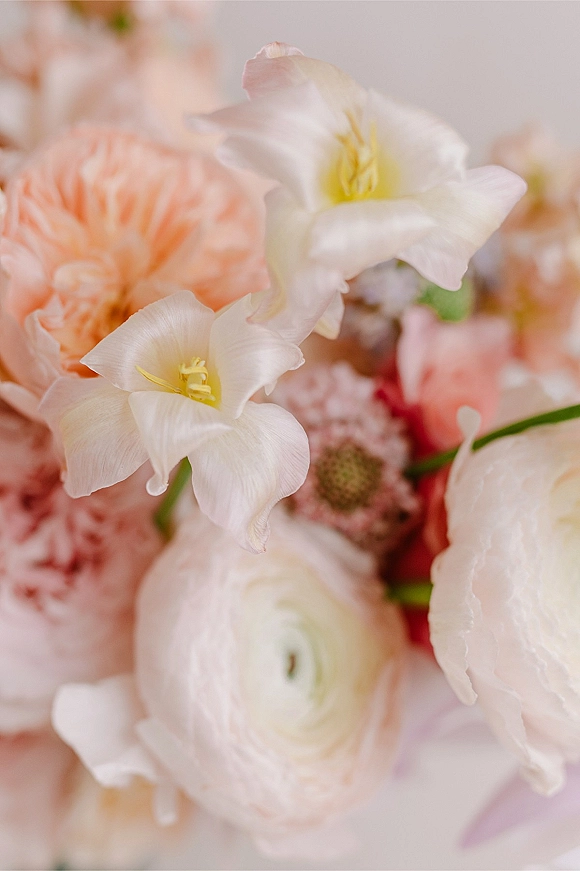 Wedding flowers in a bridal bouquet close up featuring blush, white and peach ranunculus with green stems against a soft neutral backdrop