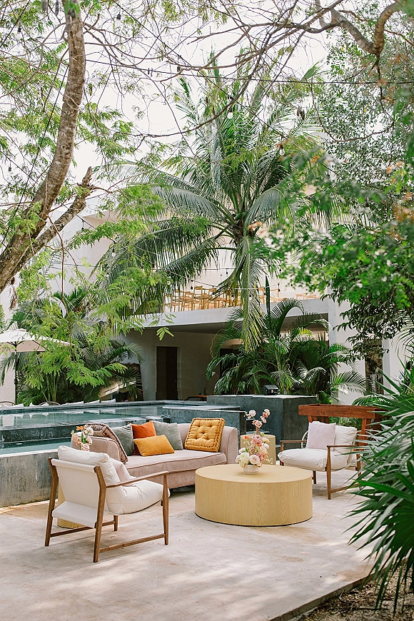 Lounge seating area with wedding lounge furniture, cream outdoor sofa and chairs around a round coffee table on a poolside deck under string lights