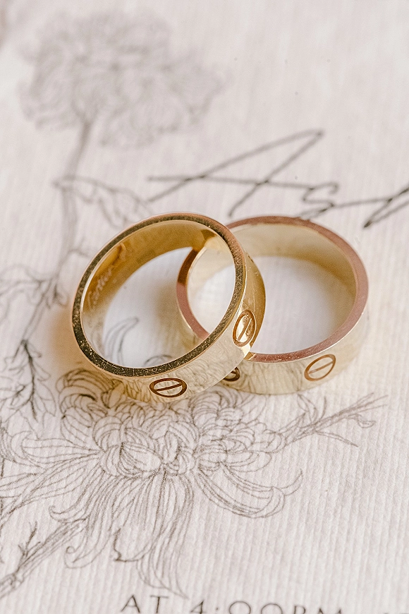 Wedding rings with gold wedding bands, engraved details, resting on illustrated paper atop a warm wood surface in a flat lay