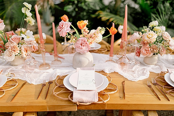 Reception tablescape with wedding table decor featuring peach florals and taper candles on a wood banquet table with greenery backdrop