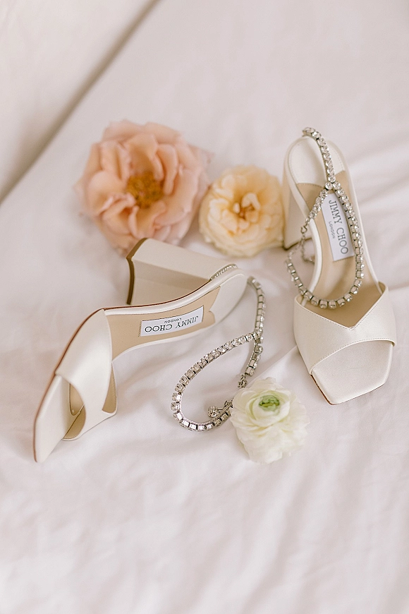 Bridal shoes, ivory wedding heels with open-toe block design and rhinestone ankle straps, styled with flowers on white fabric flat lay