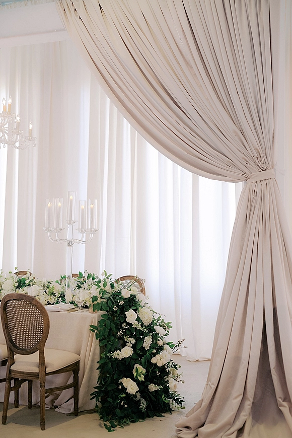 Reception tablescape at a wedding sweetheart table with white and green wedding florals, taper candles in glass candelabra, chandelier backdrop