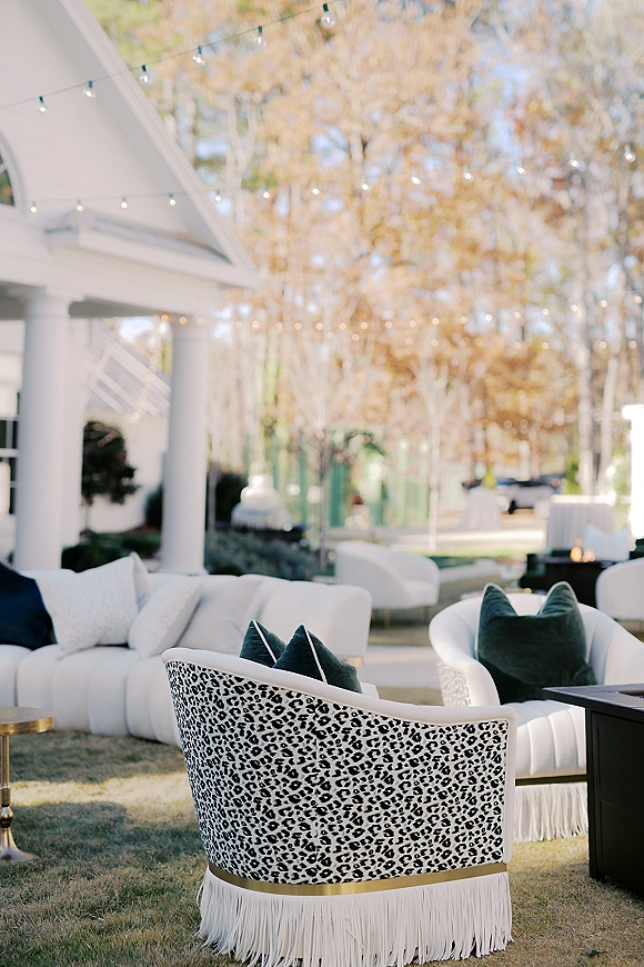 Lounge seating decor with an outdoor wedding lounge of sofas and chairs under string lights, centered around a fire pit on a lawn near a white porch