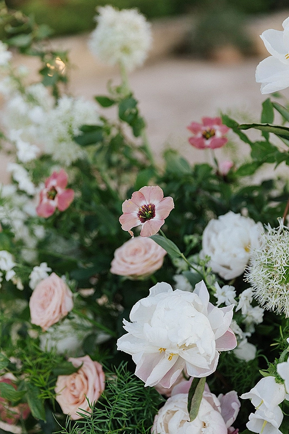 Wedding flowers in a white peony arrangement with blush roses and greenery, styled in a garden setting with a blurred walkway behind