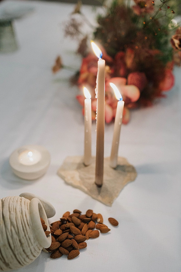 Wedding table decor with taper candle centerpiece featuring three white taper candles, tea lights, and moody florals on a white tablecloth