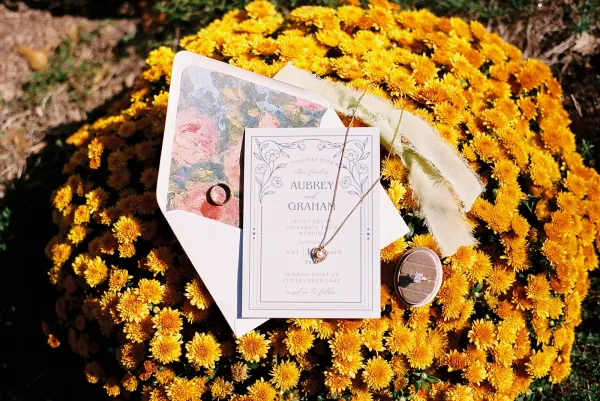 Invitation suite featuring a botanical wedding invitation with a floral envelope liner, set among yellow mums and garden greenery.