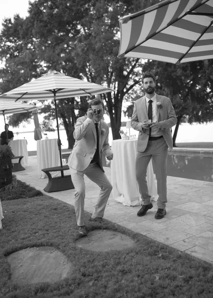 Cocktail hour moment highlighting groomsmen style, boutonnieres on lapels as they mingle by the pool and striped umbrellas on a waterfront patio.