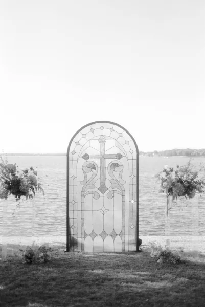 Ceremony altar with a stained glass ceremony backdrop, set on a lakeside lawn with shoreline trees and open sky, creating a serene vows setting.