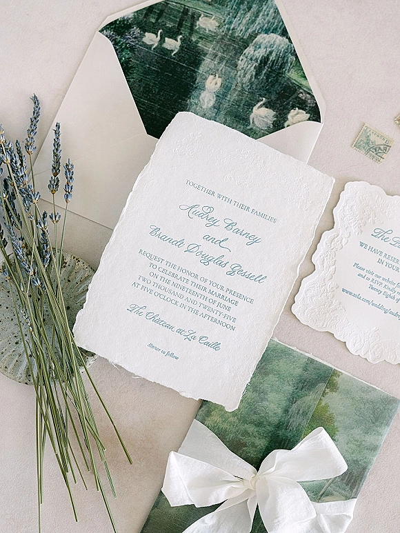 Wedding invitation suite with deckle edge invitation, embossed calligraphy cards and lavender sprigs tied with a white ribbon on neutral paper