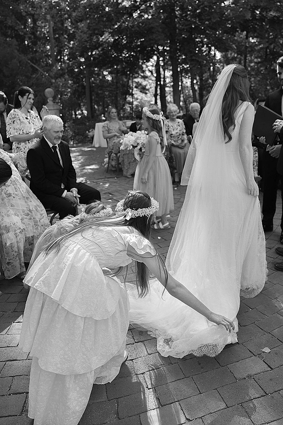 Ceremony moment at an outdoor wedding ceremony as the bride walks the brick paver aisle behind flower girls in floral crowns, long veil flowing