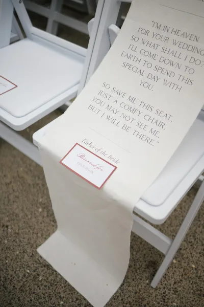 Memorial chair sign draped on a white folding chair, a save a seat sign reserved in remembrance of a loved one during the wedding ceremony.