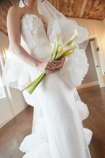 Wedding dress close-up shows a strapless wedding dress with a 3D floral bodice and ruffled tulle as the bride holds a calla lily bouquet.