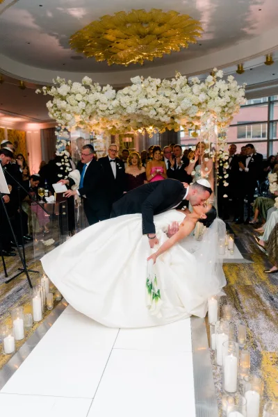 Wedding kiss during a dip kiss wedding as the groom in a kippah dips the veiled bride on a white dance floor under a floral chuppah canopy