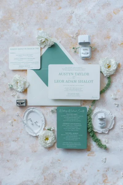 Invitation suite wedding invitation flat lay with emerald-lined envelopes, RSVP card, rings, and wax seal on textured paper with petals