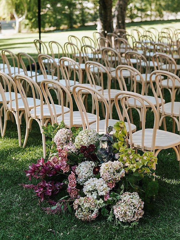 Ceremony seating with outdoor ceremony chairs in neat rows of wood bentwood chairs beside lush roses and hydrangeas on a sunny lawn with trees