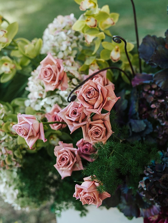 Wedding flowers with pink rose wedding flowers, green orchids and hydrangea arranged on a stand with greenery on an outdoor lawn