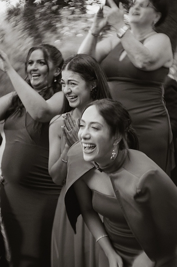 Bridesmaid reaction as bridesmaids cheering and laughing in matching dresses with statement earrings, framed by outdoor greenery