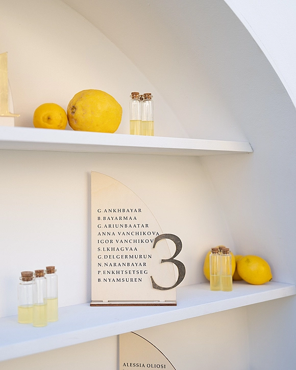 Wedding table number on an arched table number sign in an acrylic holder with wooden base and glass vials on white shelves in a niche