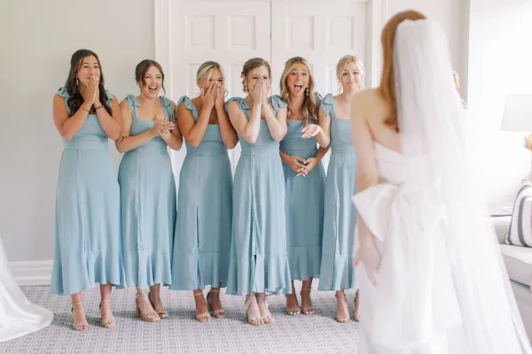 Bridesmaid reveal as bridesmaids react to the bride in a veil and strapless wedding dress, framed by white paneled doors and window light