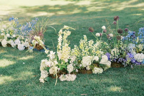 Ceremony aisle florals with grounded aisle flowers of white hydrangea, gladiolus, and blue delphinium lining a grass lawn garden setting