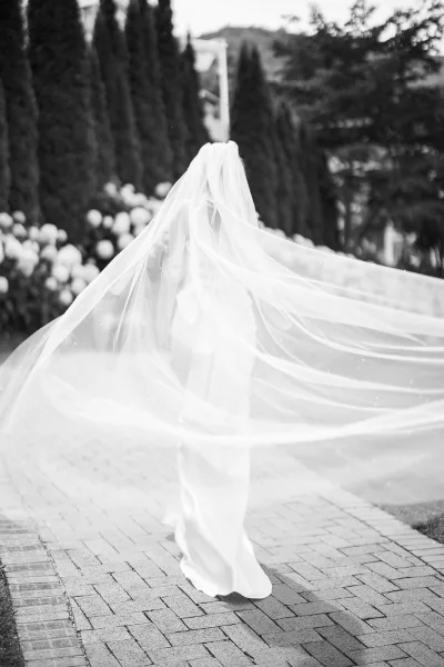 Bridal portrait in black and white of a bride from behind, walking a brick garden path in a strapless gown with veil flowing in wind