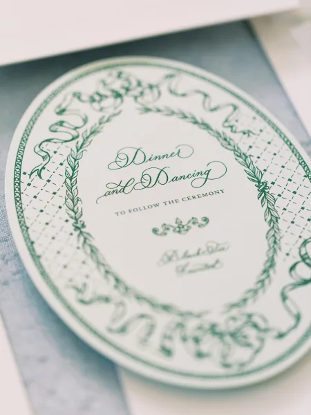 Wedding invitation with calligraphy text and ornate border, stacked with matching cards and envelope on a clean paper surface