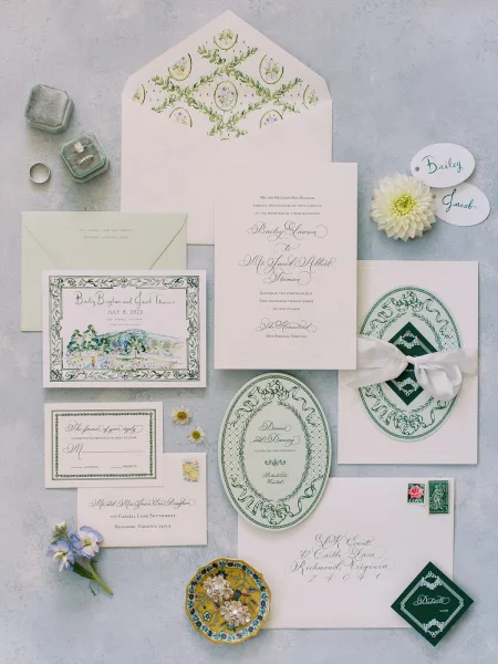 Invitation suite wedding invitation flat lay with calligraphy cards, ribbon bow, wax seal, stamps, and rings on a light gray surface