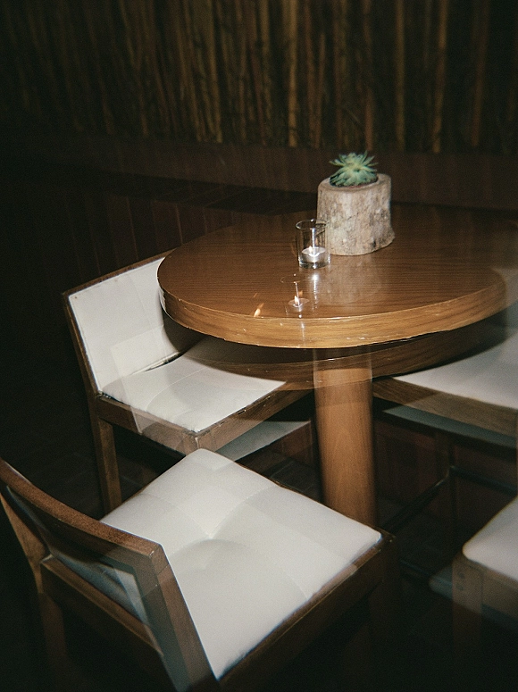Cocktail table decor in a wedding cocktail lounge with a succulent centerpiece and glass votive candle on a round wood table amid white chairs