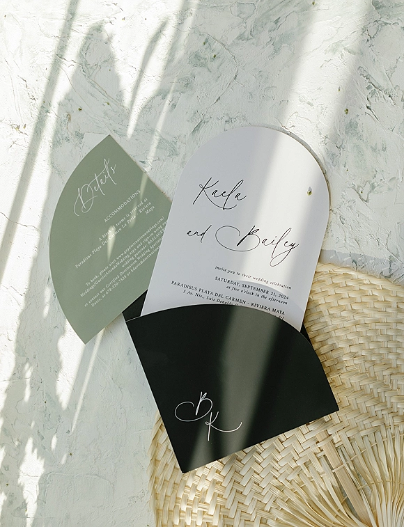 Wedding invitation suite with an arched wedding invitation, sage green details card and black envelope on textured plaster with plant shadows