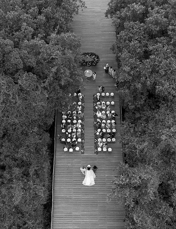 Wedding ceremony outdoor wedding ceremony seen from overhead on a wooden deck, with candle-lined aisle runner, chairs, and a round floral arch amid trees