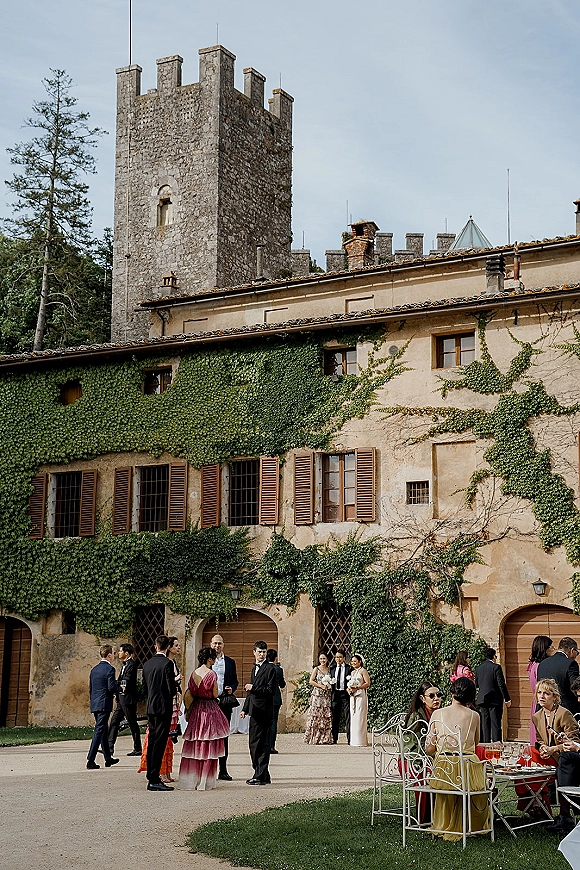 Wedding cocktail hour with outdoor wedding cocktails as guests mingle by lounge chairs and tables in an ivy-covered courtyard by a stone tower