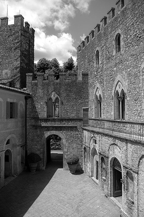 Wedding venue exterior with stone walls and arched doorways, iron railing and potted plants in a historic courtyard under cloudy sky
