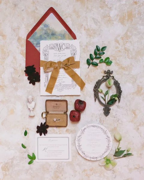 Invitation suite wedding invitation flat lay with velvet ribbon and wax seal, rings and florals arranged on a neutral stone surface