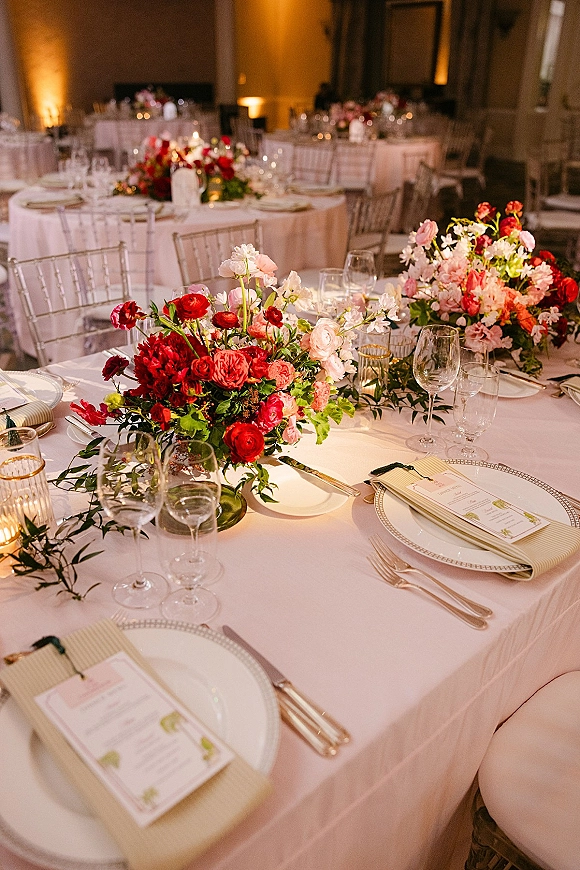 Reception tablescape with round wedding tables, blush linens, floral centerpieces and greenery garland, candlelight and warm uplighting in a ballroom